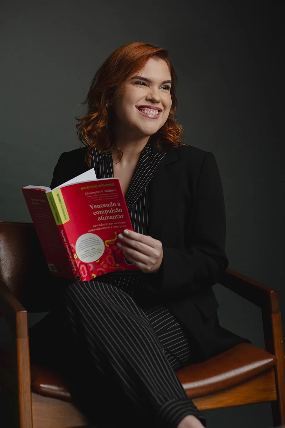 Dra. Mariana Barbalho sorrindo, sentada, com o livro Vencendo a compulsão alimentar